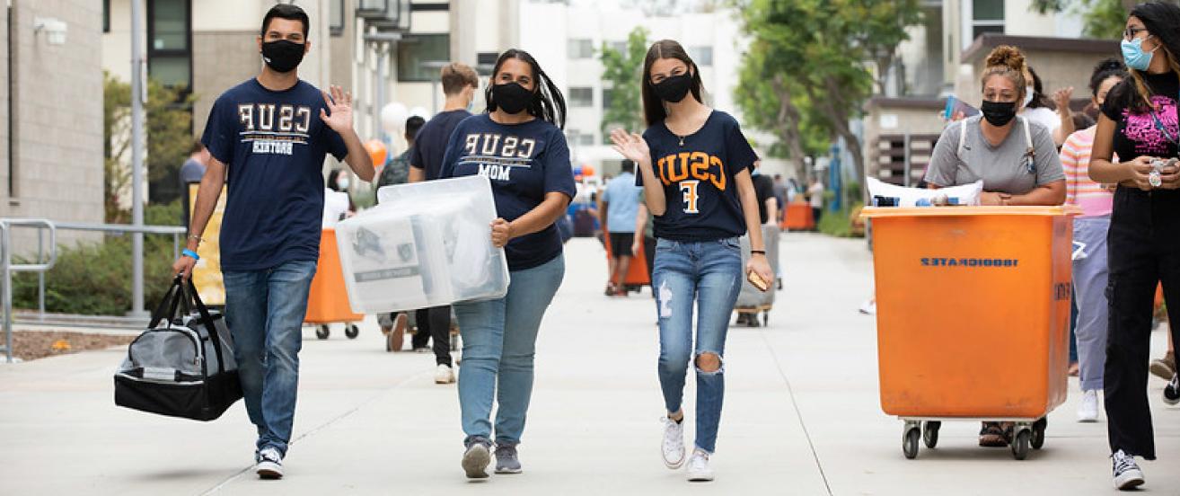 Students waving and walking as they move in to their dorms. 